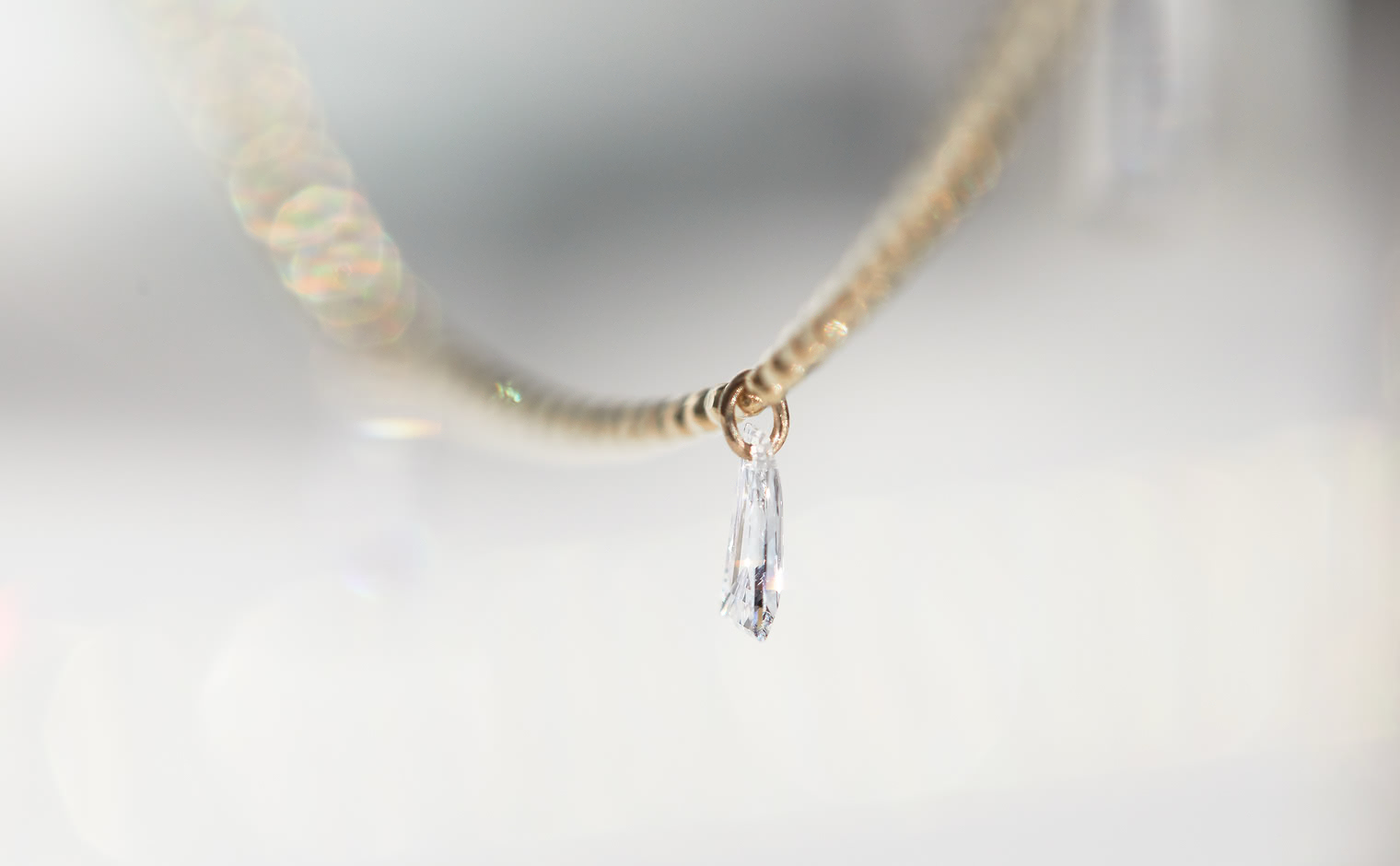 Tapered Diamond Necklace by kataoka, a single elongated diamond suspended from a hoop on a beige gold chain, showing the laser-drilled floating diamond mechanism