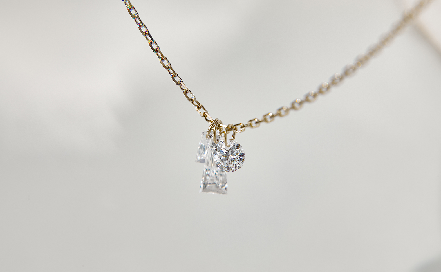 Tassel Round Diamond Necklace by kataoka, diamonds hanging freely from hoops on a fine beige gold chain, suspended against a soft background