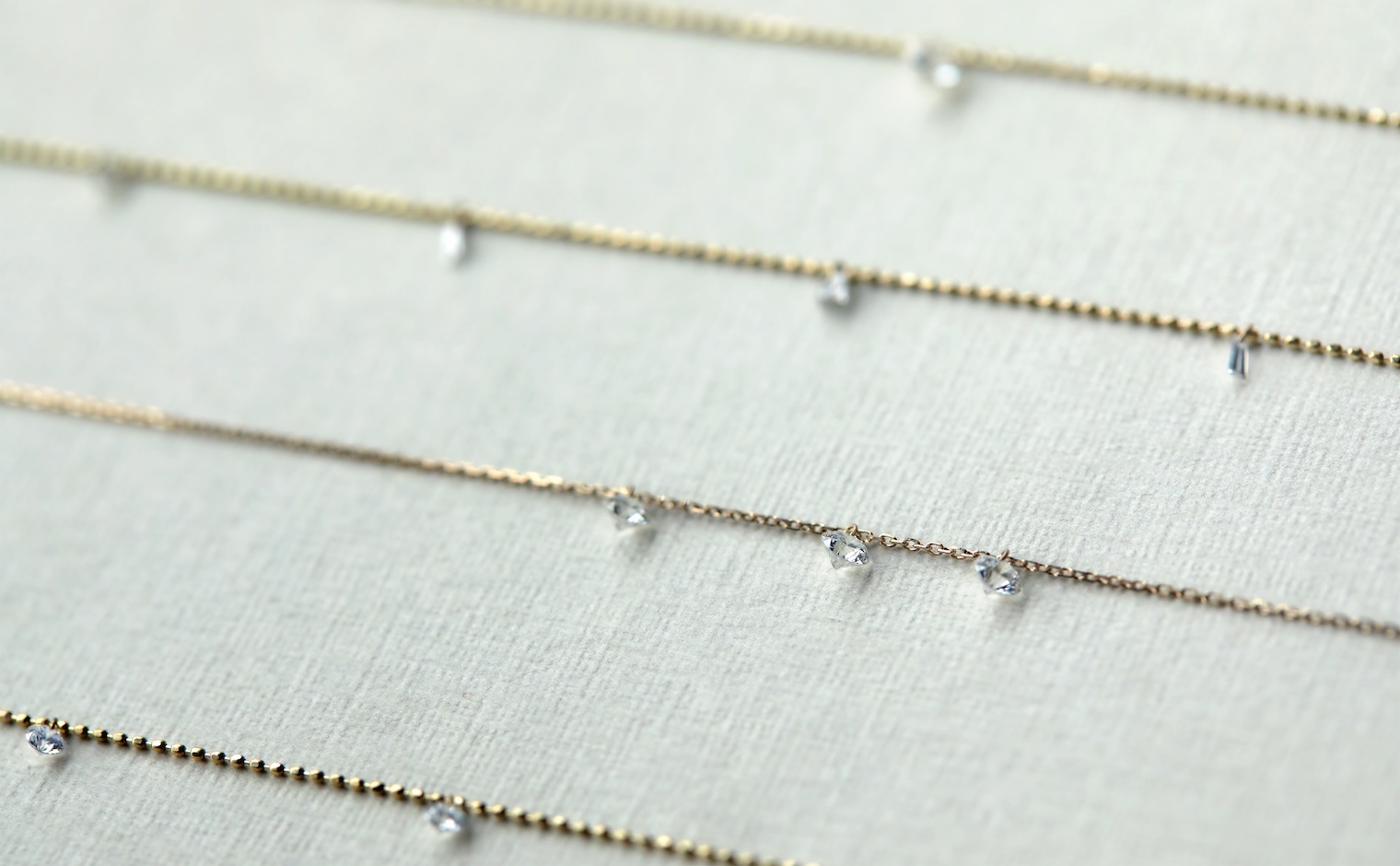 kataoka Less is More necklaces laid side by side on a neutral surface, each chain carrying floating diamonds in different cuts